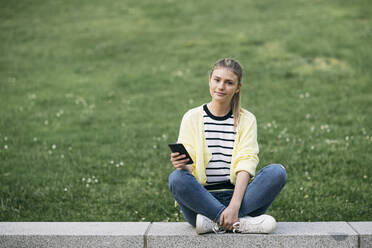 Woman with her phone sitting in public park - ABZF03422