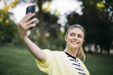 Frau lächelt, während sie ein Selfie in einem öffentlichen Park macht - ABZF03424