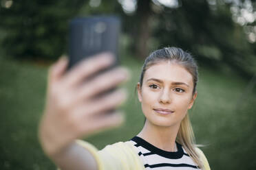 Mittlere erwachsene Frau, die ein Selfie mit ihrem Smartphone macht, während sie in einem öffentlichen Park steht - ABZF03426