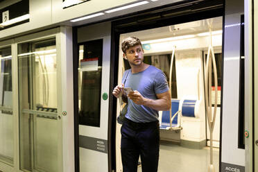 Gut aussehender junger männlicher Pendler, der beim Aussteigen aus einem U-Bahn-Zug am Bahnhof wegschaut - VABF03592