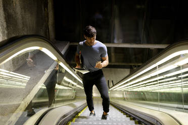 Männlicher Pendler, der sein Smartphone benutzt, während er auf einer Rolltreppe in der U-Bahn steht - VABF03594