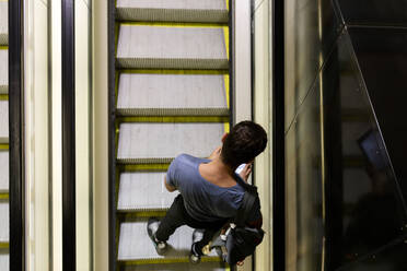 Mann benutzt Smartphone, während er auf einer Rolltreppe in einer beleuchteten U-Bahn steht - VABF03596