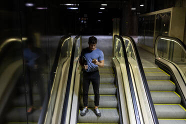 Young man using smart phone while holding digital tablet on escalator at subway - VABF03597