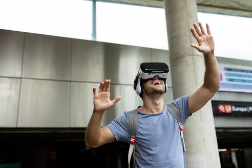 Lächelnder junger männlicher Pendler, der ein Virtual-Reality-Headset in einer U-Bahn-Station benutzt - VABF03608