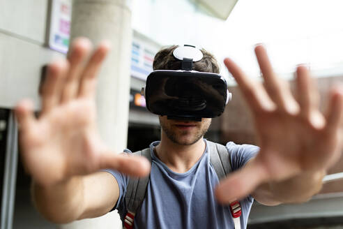 Junger Mann gestikuliert, während er ein Virtual-Reality-Headset in einer U-Bahn-Station benutzt - VABF03609