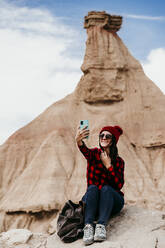 Spanien, Navarra, Porträt einer Touristin, die ein Selfie vor einer Sandsteinfelsformation in Bardenas Reales macht - EBBF00848