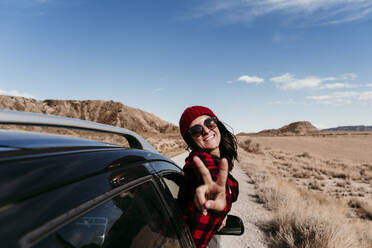 Spain, Navarre, Portrait of female tourist leaning out of car window making peace sign toward camera - EBBF00857