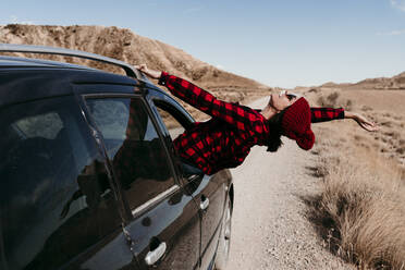 Spain, Navarre, Female tourist leaning out of car window over dirt road in Bardenas Reales - EBBF00858