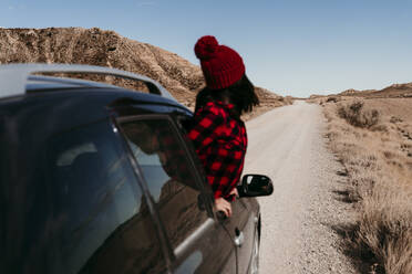 Spanien, Navarra, Weibliche Touristin lehnt sich aus dem Autofenster über dem Feldweg in Bardenas Reales - EBBF00859