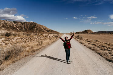 Spain, Navarre, Female tourist standing with raised arms in middle of empty dirt road in Bardenas Reales - EBBF00861