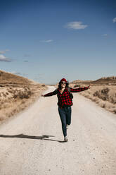 Spain, Navarre, Female tourist running toward camera along empty dirt road in Bardenas Reales - EBBF00866