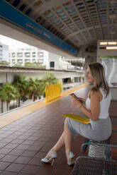 Female commuter looking away while sitting on bench at railroad station - MAUF03550