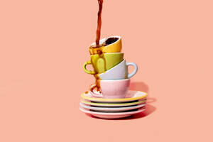 Studioaufnahme von Kaffee, der auf einen Stapel von Tellern und Kaffeetassen gegossen wird - GEMF04210