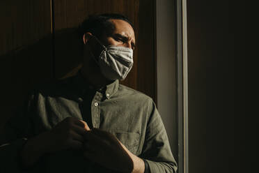 Man wearing protective face mask while looking away at home - DSIF00177