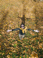 Smiling beautiful woman with arms outstretched enjoying autumn at park - KNTF05678