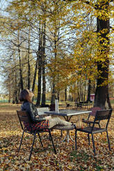 Frau, die an einem sonnigen Tag im Park sitzt und nach oben schaut - KNTF05691