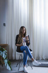 Geschäftsfrau, die ein Smartphone benutzt, während sie im Büro Kaffee trinkt - DCRF00925