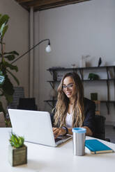 Smiling businesswoman using laptop at desk in office - DCRF00926