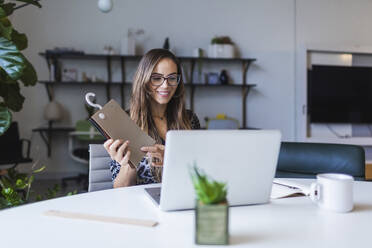 Creative businesswoman showing fabric swatch while video calling through laptop - DCRF00931