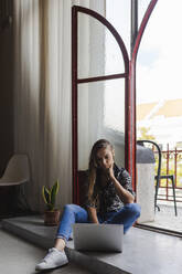 Female entrepreneur working on laptop while sitting at doorway in creative office - DCRF00937