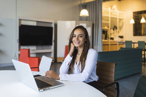 Selbstbewusste Geschäftsfrau mit Laptop am Schreibtisch im Büro - DCRF00943