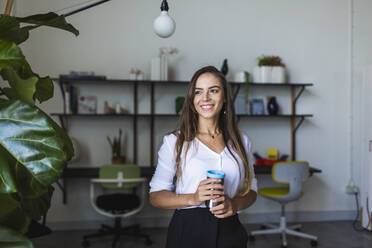 Lächelnde Geschäftsfrau mit isoliertem Kaffeebecher im Büro - DCRF00953