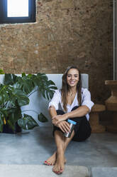 Lächelnde Geschäftsfrau mit isoliertem Kaffeebecher auf dem Boden im Büro sitzend - DCRF00954