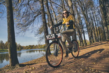 Lächelnde Frau auf dem Fahrrad im Park an einem sonnigen Tag - KNTF05709