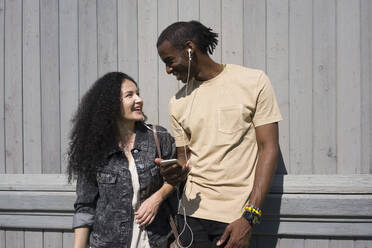 Couple listening music while standing against wall - VPIF03085