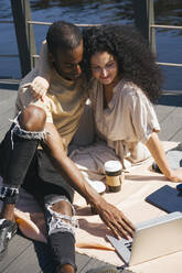 Couple using laptop while sitting on bridge in city - VPIF03087