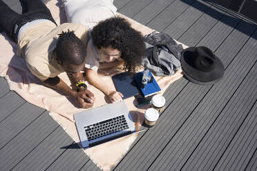 Man and woman using laptop while lying on bridge path at city - VPIF03090