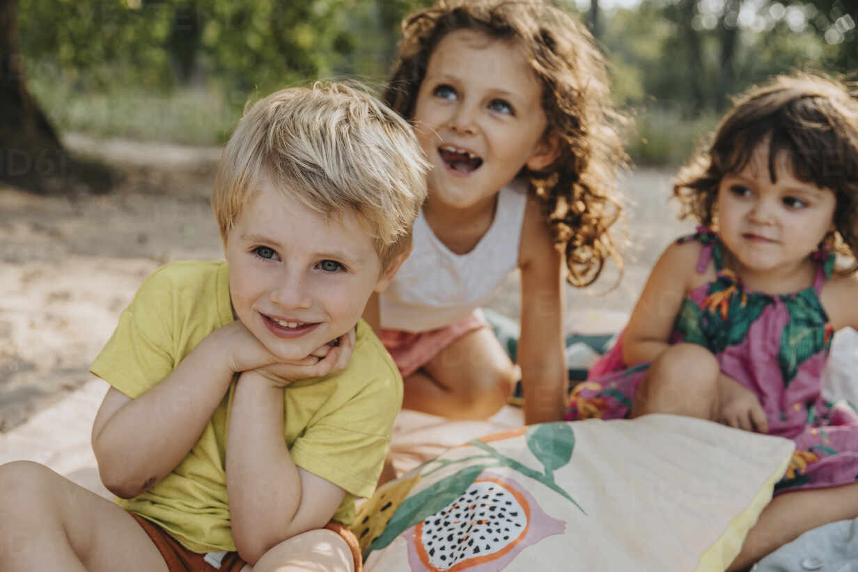 Aufgeregte Kinder Mit Hand Am Kinn Und Offenem Mund Am Strand Sitzend Lizenzfreies Stockfoto 