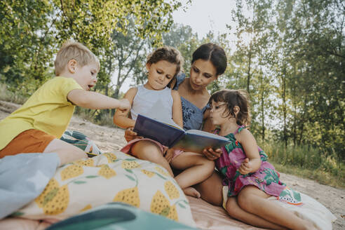 Ältere Frau und drei Kinder lesen ein Buch am Strand - MFF06235