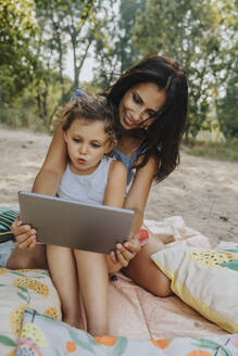 Mutter und Tochter benutzen digitales Tablet am Strand - MFF06239