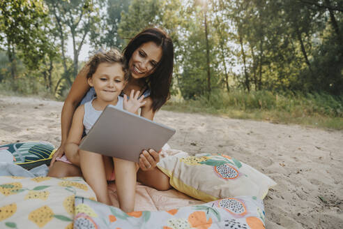 Mutter und Tochter machen einen Videoanruf am Strand an einem sonnigen Tag - MFF06240