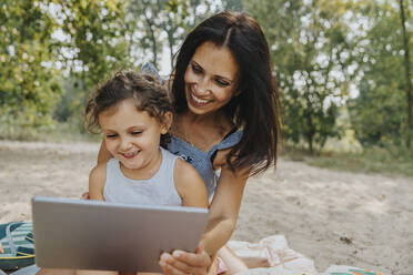 Lächelnde Mutter und Tochter mit digitalem Tablet am Strand - MFF06241