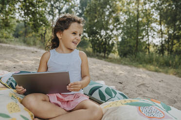 Lächelndes süßes Mädchen, das wegschaut und ein digitales Tablet hält - MFF06242