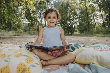 Nettes Mädchen liest Buch, während sie am Strand an einem sonnigen Tag sitzt - MFF06243