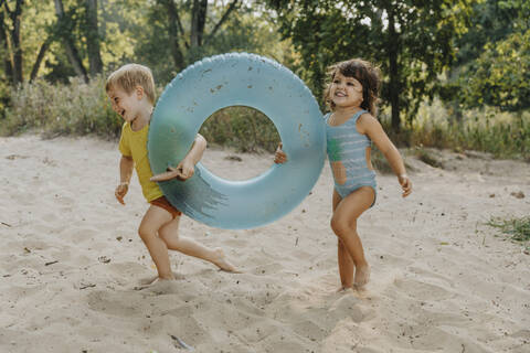 Children running with inflatable ring at beach stock photo