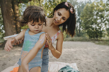 Mother applying sunscreen to daughter at beach - MFF06245