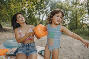 Mother putting swimmies to daughter at beach - MFF06247