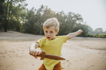 Niedlicher kleiner Junge spielt mit Holzdolch am Strand - MFF06251