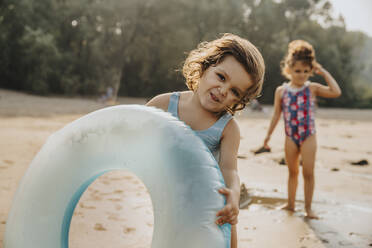 Geschwisterkind mit aufblasbarem Ring am Strand stehend - MFF06252