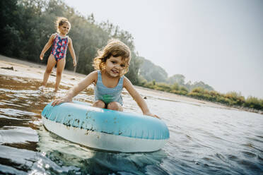 Schwestern genießen im Wasser mit aufblasbaren Ring am sonnigen Tag - MFF06254