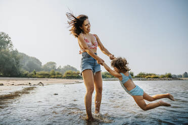Mother whirling daughter around while standing in water at beach - MFF06255