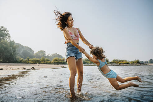 Mutter wirbelt Tochter herum, während sie am Strand im Wasser steht - MFF06255