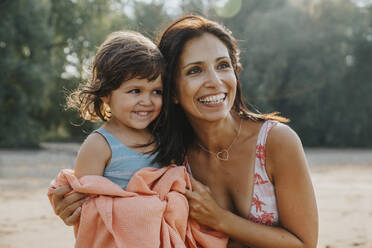 Lächelnde Mutter legt Handtuch um ihre Tochter am Strand - MFF06263