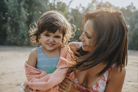 Mother putting towel around daughter at beach on sunny day stock photo