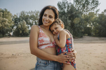 Mutter und Tochter umarmen sich, während sie am Strand stehen - MFF06268