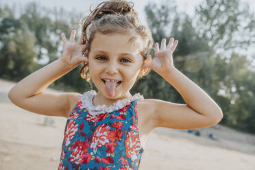 Niedliches kleines Mädchen streckt die Zunge heraus, während es am Strand steht - MFF06270